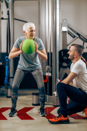 Téléchargez les photos : Femme âgée fait de l'entraînement avec un entraîneur personnel dans la salle de gym. - en image libre de droit