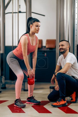 Foto de Mujer joven está haciendo ejercicios con kettlebell durante el entrenamiento con entrenador personal en el gimnasio. - Imagen libre de derechos