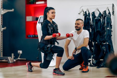 Foto de Young woman is doing EMS personal training with coach in the gym. - Imagen libre de derechos