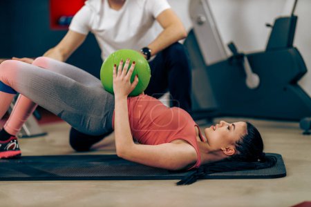 Foto de Mujer joven está haciendo entrenamiento para abdominales con entrenador personal en un gimnasio. - Imagen libre de derechos