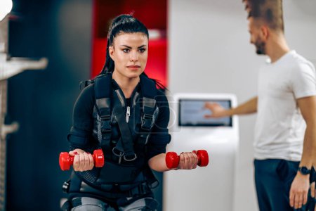 Foto de Young woman is doing EMS personal training with coach in the gym. - Imagen libre de derechos