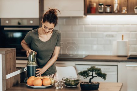 Téléchargez les photos : Young woman daydreaming while enjoying morning and preparing a healthy smoothie at home. - en image libre de droit