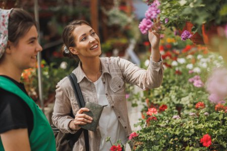Téléchargez les photos : Une jeune femme qui choisit et achète des plantes et des fleurs auprès d'une jeune entrepreneure dans un centre de jardinage. - en image libre de droit
