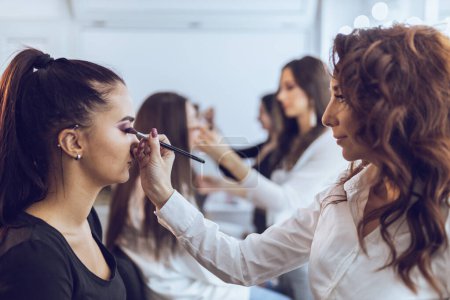 Photo for Girls are attending the make up masterclass. They are training on the model how to do perfect makeup. - Royalty Free Image