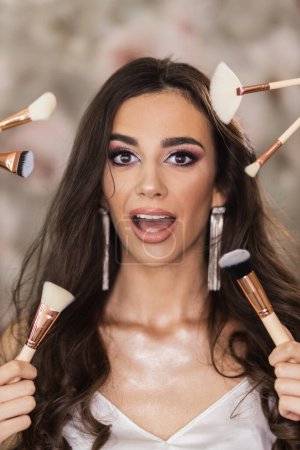 Téléchargez les photos : Portrait d'une belle jeune femme entourée de pinceaux de maquillage qui présente un joli maquillage sur son visage. - en image libre de droit