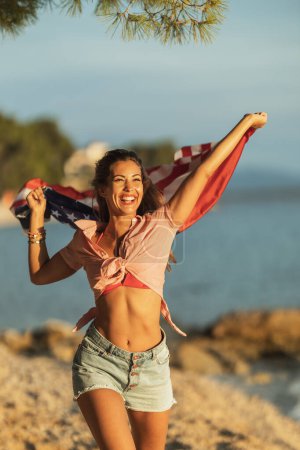 Foto de Happy young woman with US national flag having fun and spending the day on the beach. - Imagen libre de derechos