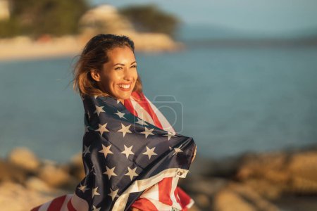 Photo for Smiling young woman with US national flag enjoying a relaxing day on the beach. - Royalty Free Image