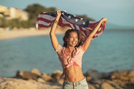 Téléchargez les photos : Attractive young woman with US national flag having fun and relaxing day on the beach. - en image libre de droit