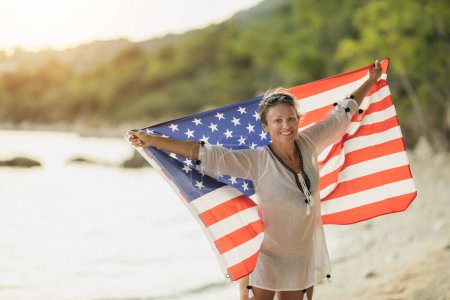 Photo for An attractive middle age woman with American national flag enjoying a relaxing day on the beach. - Royalty Free Image