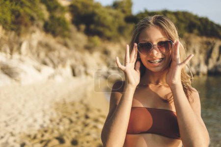 Téléchargez les photos : Jolie adolescente souriante avec des lunettes de soleil en forme de coeur profitant de vacances d'été sur la plage. - en image libre de droit