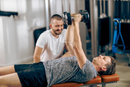 Téléchargez les photos : Middle age man is doing training with personal trainer in a gym. - en image libre de droit