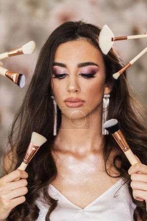 Photo for A portrait of a beautiful young woman surrounded by makeup brushes who is presenting a nice makeup on her face. - Royalty Free Image