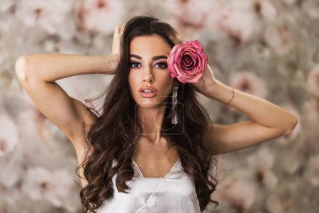 Photo for A portrait of an attractive woman with pink rose in her hair who is looking at camera - Royalty Free Image