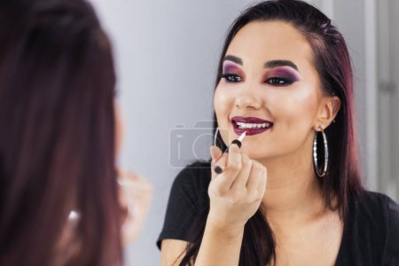 Téléchargez les photos : Jeune femme mignonne applique gloss lèvres devant le miroir. Focus sur la réflexion dans le miroir. - en image libre de droit