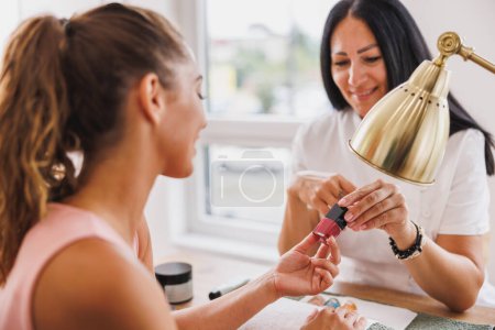 Téléchargez les photos : Jeune femme assise à travers esthéticienne et choisir la couleur des ongles dans un salon de beauté. - en image libre de droit