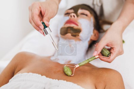 Photo for Woman getting a gua sha treatment with a jade roller on decollete zone at the beauty salon. - Royalty Free Image