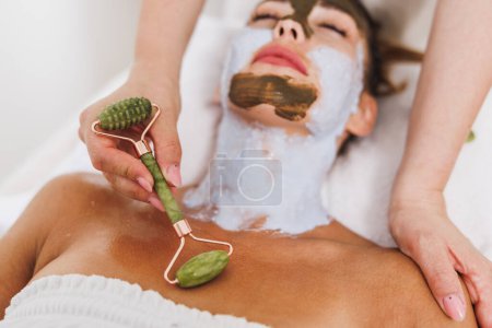 Téléchargez les photos : Femme obtenir un traitement gua sha avec un rouleau de jade sur la zone décollete au salon de beauté. - en image libre de droit