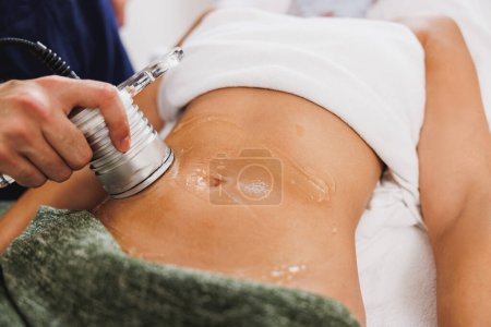 Téléchargez les photos : Femme méconnaissable obtenir un traitement de cavitation échographie à la réduction de la graisse sur l'abdomen au salon de beauté. - en image libre de droit