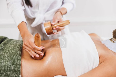 Photo for An unrecognizable woman getting anti cellulite maderotherapy massage with wooden cup at the beauty salon. - Royalty Free Image