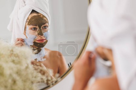 Téléchargez les photos : Belle jeune femme en face du miroir enlever le masque facial au salon de beauté spa. - en image libre de droit