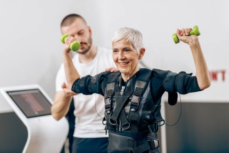 Téléchargez les photos : Senior woman is doing EMS training with personal trainer in the gym. - en image libre de droit