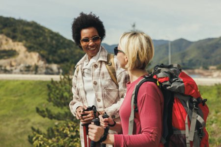 Photo for Two female friends with backpack talking while hiking in mountains. - Royalty Free Image