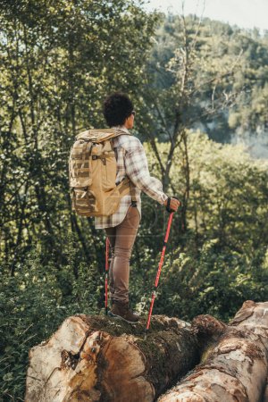 Photo for Rear view of a black woman with backpack and trekking poles hiking in mountains. - Royalty Free Image