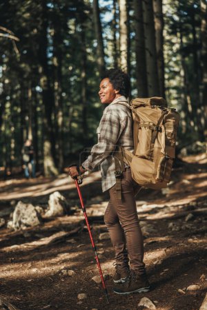 Photo for Mature black woman with backpack and trekking poles hiking alone in mountains. - Royalty Free Image