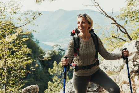 Foto de Madura sonriente mujer de pie en la cima de una colina y disfrutar de la vista durante su caminata en las montañas. - Imagen libre de derechos