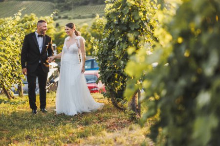 Foto de Foto de una feliz pareja joven caminando en el viñedo en el día de su boda. - Imagen libre de derechos