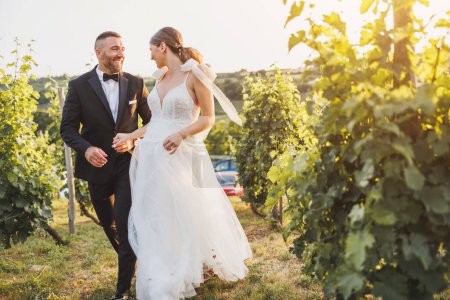 Foto de Foto de una feliz pareja joven caminando en el viñedo al atardecer en el día de su boda. - Imagen libre de derechos