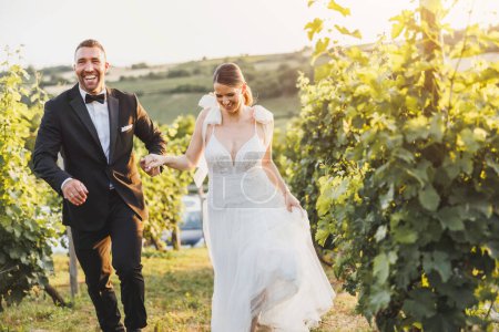 Foto de Una joven y feliz pareja de novios divirtiéndose y corriendo en el viñedo al atardecer. - Imagen libre de derechos