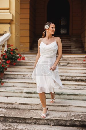 Foto de Hermosa novia en vestido de novia blanco hermoso caminando camina por las escaleras al aire libre en el día de su boda. - Imagen libre de derechos
