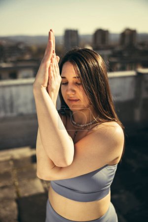 Téléchargez les photos : Close-up of a young  relaxed woman practicing yoga on a rooftop terrace. - en image libre de droit