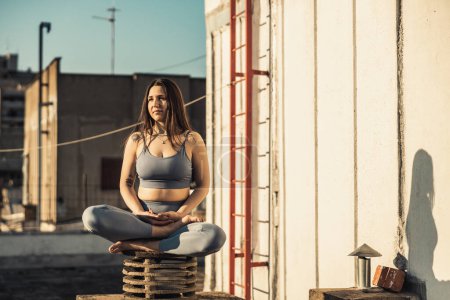 Foto de Relaxed woman practicing yoga meditating on a rooftop terrace. - Imagen libre de derechos