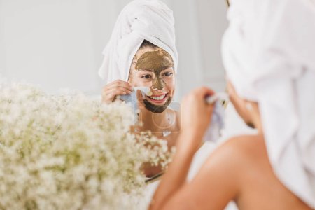 Foto de Hermosa joven frente al espejo quitando la máscara facial en el salón de spa de belleza. - Imagen libre de derechos