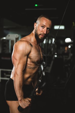 Foto de Un joven musculoso fisicoculturista haciendo entrenamiento duro para los músculos de sus brazos en el gimnasio. - Imagen libre de derechos