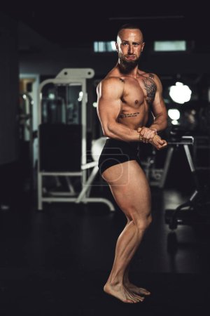 Foto de Foto de un joven musculoso culturista mostrando sus músculos perfectos mientras posaba después de hacer ejercicio en el gimnasio. - Imagen libre de derechos