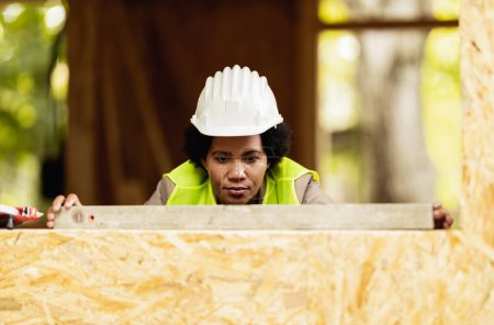 Téléchargez les photos : Prise de vue d'une architecte afro-américaine utilisant le niveau de la fenêtre lors de la vérification du chantier d'une nouvelle maison en bois. - en image libre de droit