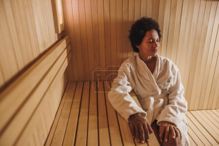 Téléchargez les photos : Belle femme mûre afro-américaine se relaxant dans un sauna au centre de spa. - en image libre de droit