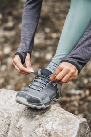 Foto de Primer plano de una mujer negra irreconocible atando sus zapatillas en el bosque durante el senderismo o trotando en la montaña. - Imagen libre de derechos