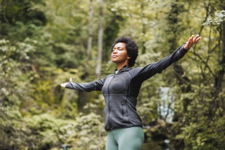 Photo for Black woman standing in nature with arms outstretched and enjoying in fresh air. - Royalty Free Image