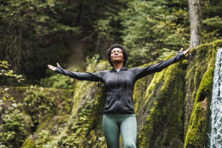 Foto de Mujer negra de pie en la naturaleza con los brazos extendidos y disfrutando al aire libre. - Imagen libre de derechos