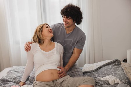 Téléchargez les photos : Joyeux couple enceinte se détendre sur un lit dans la chambre. - en image libre de droit