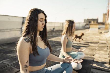 Téléchargez les photos : Two young women practicing yoga on a rooftop terrace. - en image libre de droit