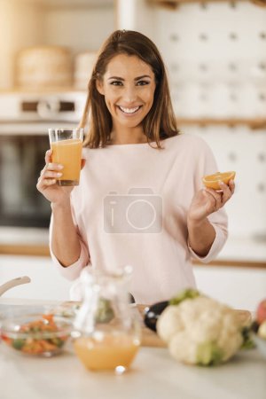 Foto de Foto de una joven sonriente bebiendo jugo de naranja fresco en su cocina. - Imagen libre de derechos