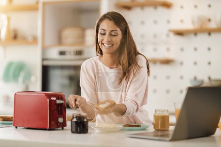 Téléchargez les photos : Tourné d'une jeune femme souriante préparant le petit déjeuner pour elle-même dans la cuisine à la maison. - en image libre de droit