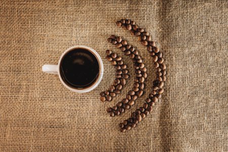 Foto de Granos de café tostados frescos en forma de W-iFi y taza de café caliente en una bolsa de arpillera sobre la mesa . - Imagen libre de derechos
