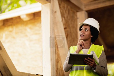 Téléchargez les photos : Portrait d'une femme architecte afro-américaine utilisant une tablette numérique et vérifiant le chantier d'une nouvelle maison en bois. - en image libre de droit
