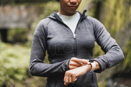 Téléchargez les photos : Gros plan d'une femme noire méconnaissable regardant smartwatch et se préparant à faire du jogging dans la nature. - en image libre de droit